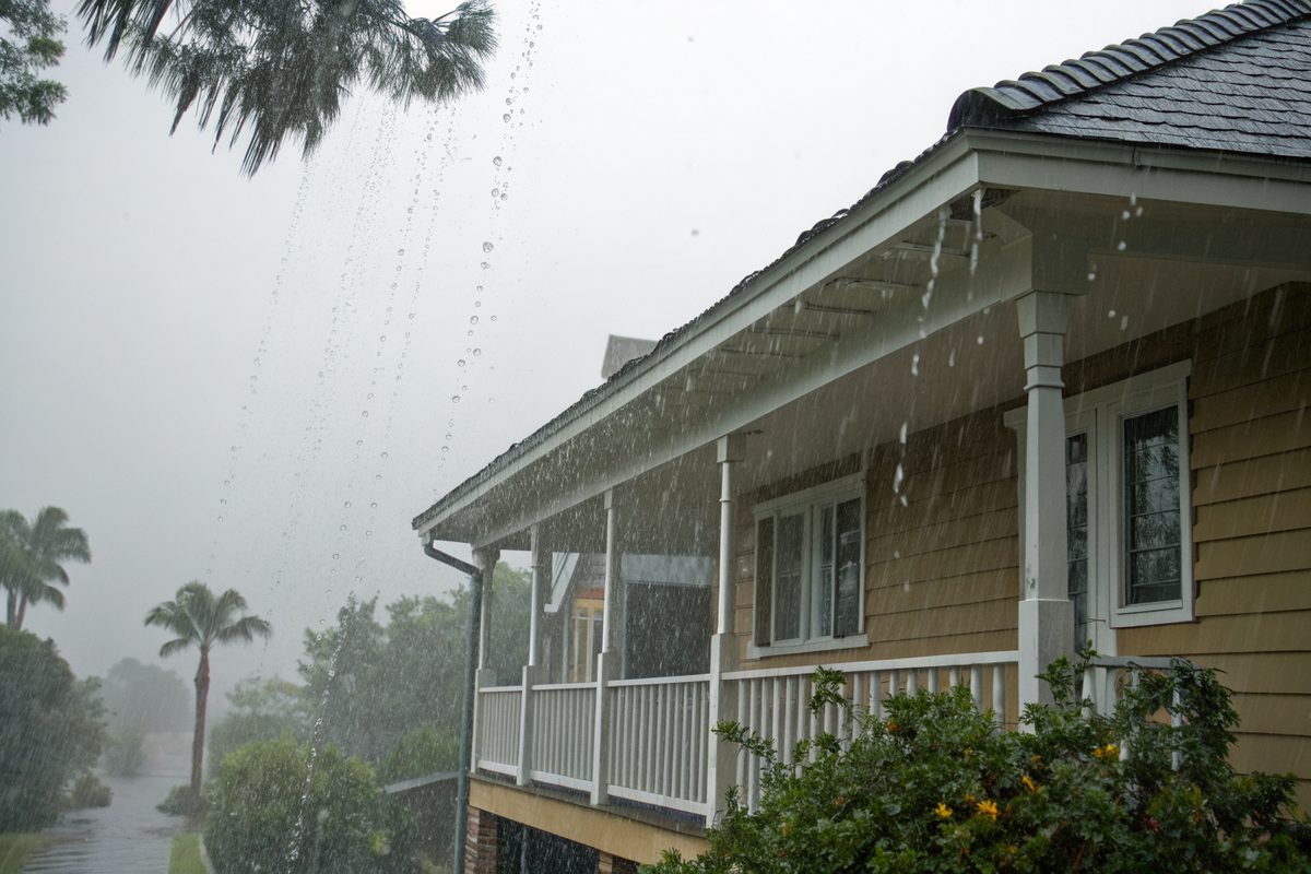 Heavy rain running off the roof edge and porch of a raised house during a tropical storm